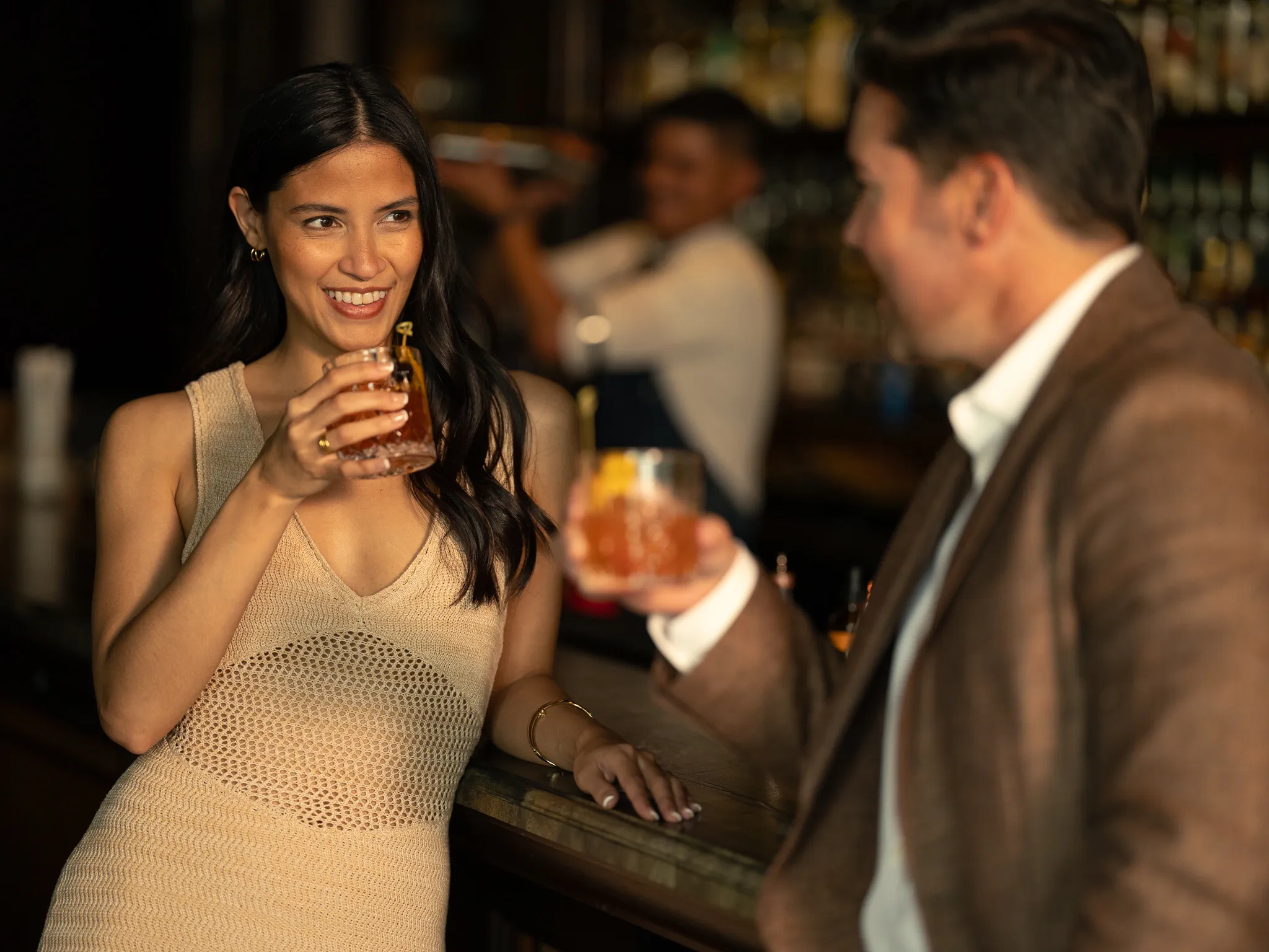 A guest smiles over a cocktail at the bar