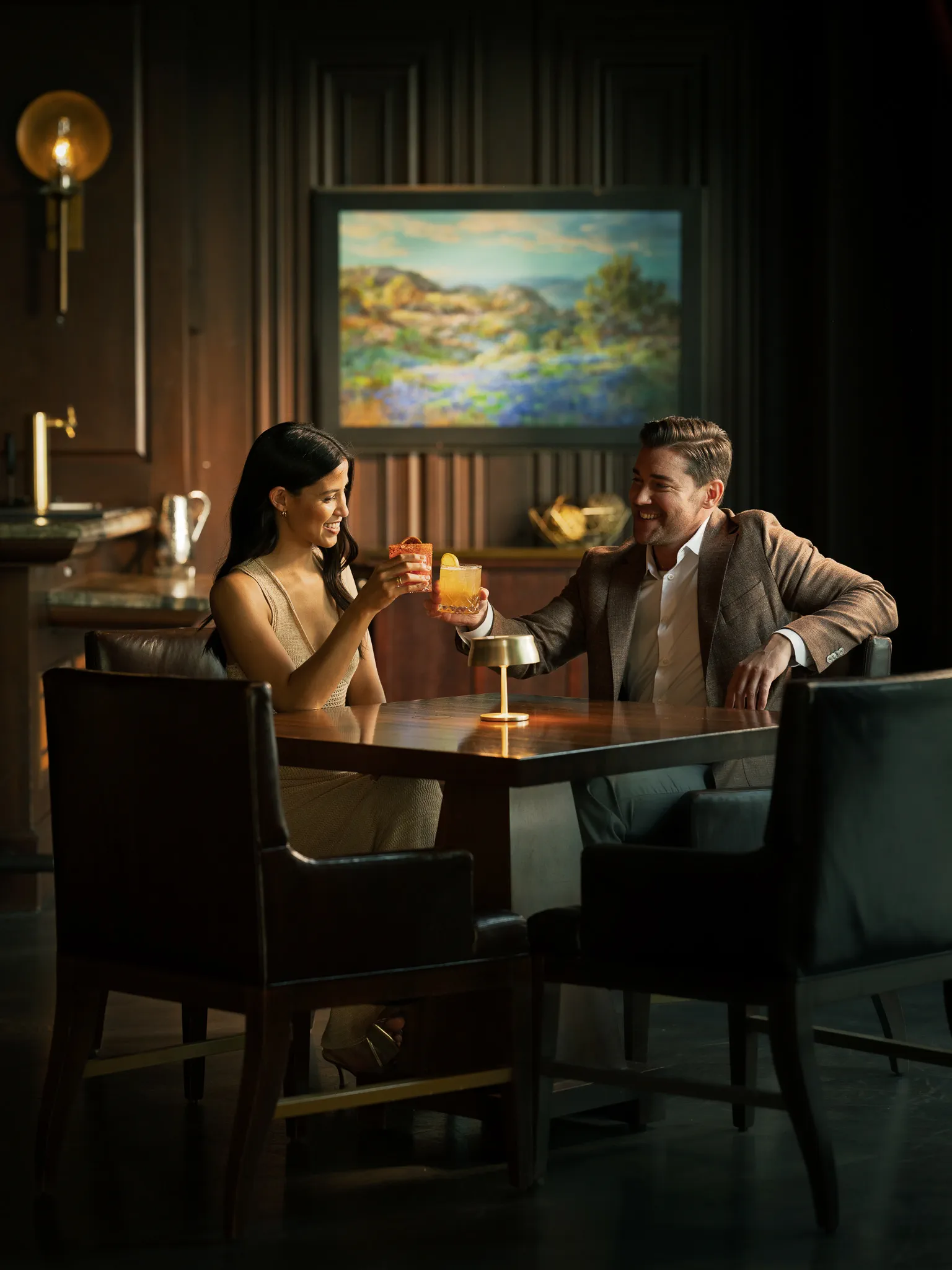 A couple toasts cocktails in a wood-panelled bar
