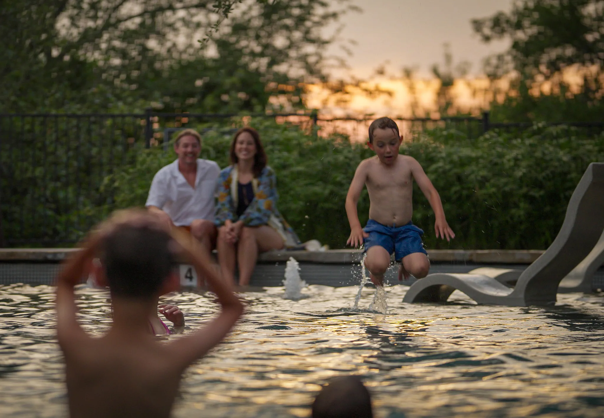A boy jumps into the resort pool as his parents watch at sunset