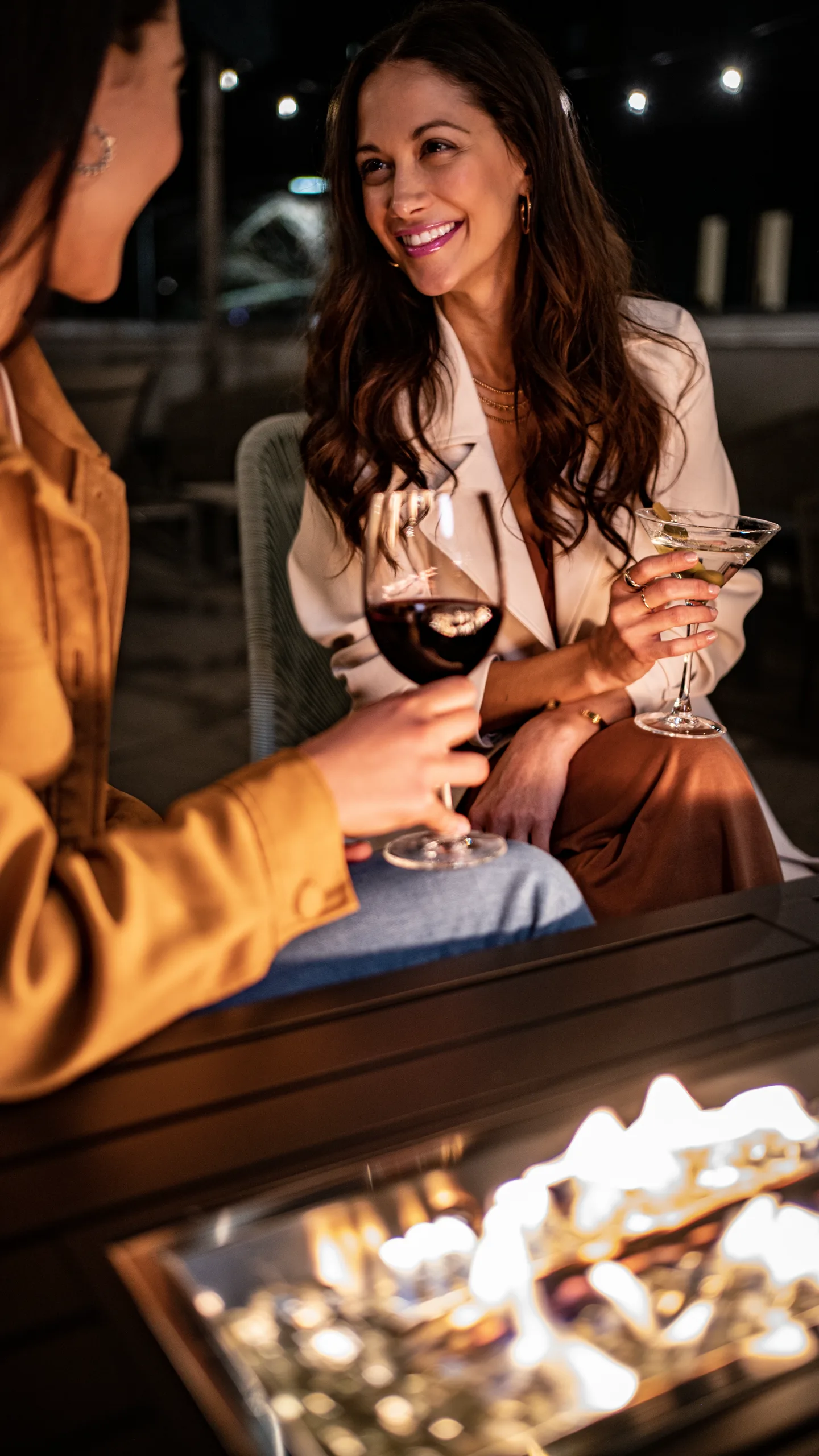 Two guests talk over drinks by the fire pit